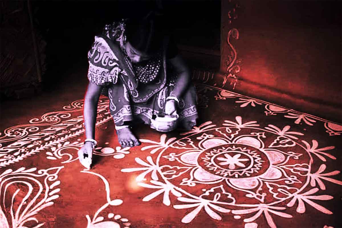 Woman drawing traditional alpana patterns with rice paste on the floor